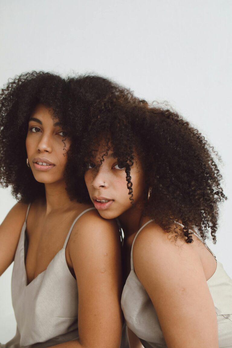 Elegant portrait of two young black women with natural afro hair, posing together indoors.